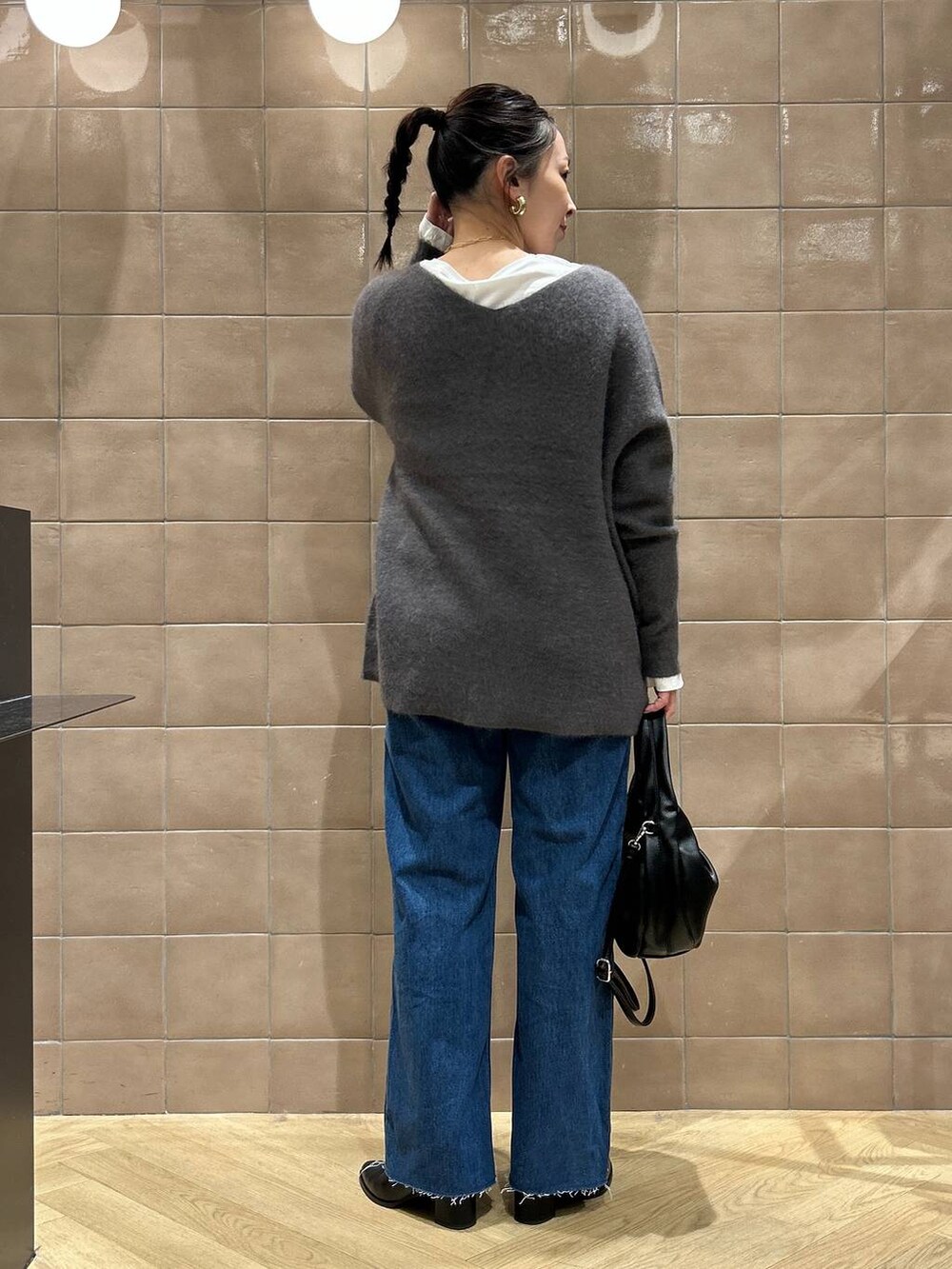 グレー系のニット/セーター、ブルー系のデニムパンツ、ブラック系のハンドバッグを着用したレディースの秋コーディネートの4枚目の写真