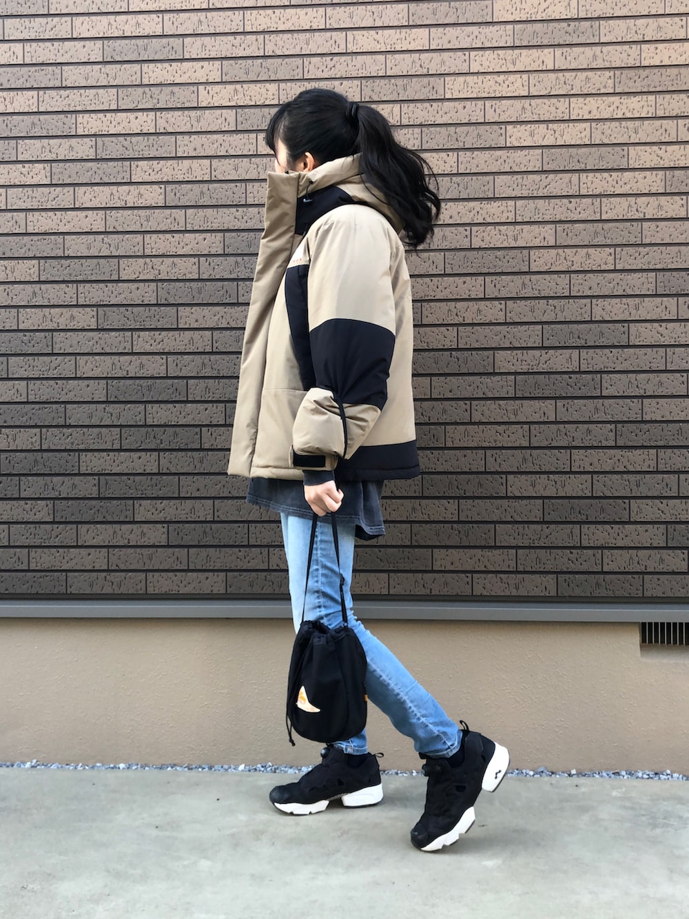 ブラック系のショルダーバッグ、ブルー系のデニムパンツ、ブラック系のスニーカーを着用したレディースの冬コーディネートの2枚目の写真