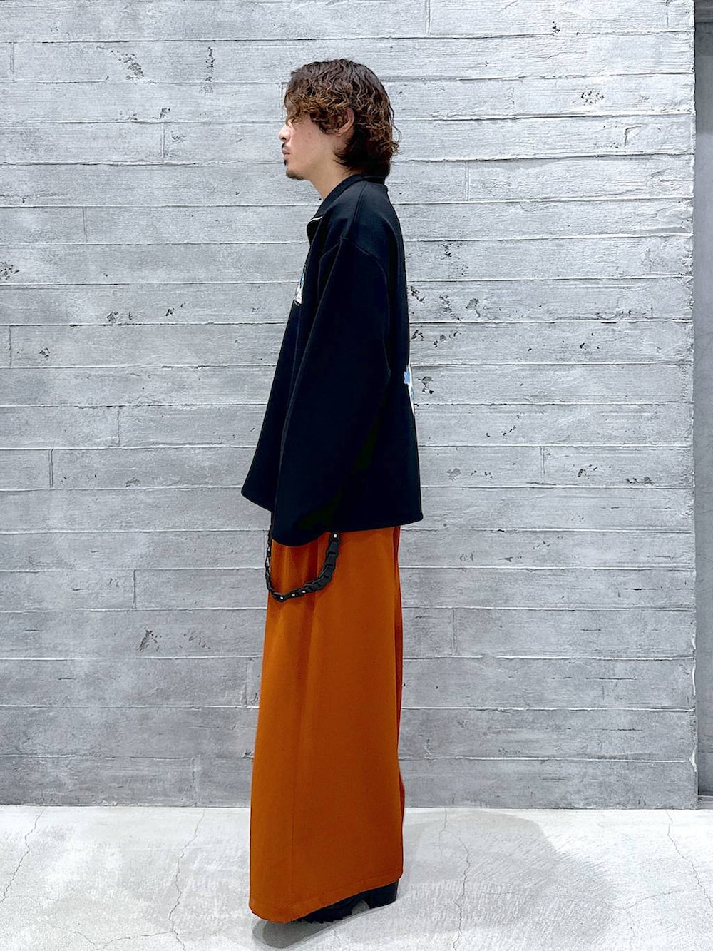 オレンジ系のスラックス、ブラック系のドレスシューズ、ブラック系のTシャツ/カットソーを着用したメンズの春コーディネートの2枚目の写真