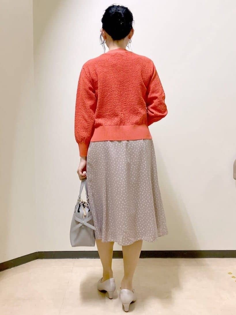 オレンジ系のニット/セーター、ブラウン系のスカート、ベージュ系のトレンチコートを着用したレディースの春コーディネートの3枚目の写真