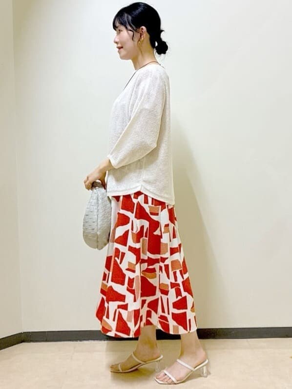 ベージュ系のニット/セーター、オレンジ系のワンピース、ベージュ系のハンドバッグを着用したレディースの夏コーディネートの2枚目の写真