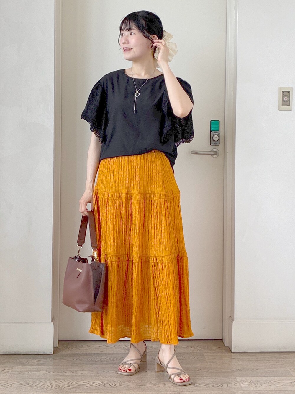 ブラック系のシャツ/ブラウス、オレンジ系のスカート、ベージュ系のブルゾンを着用したレディースの夏コーディネートの6枚目の写真