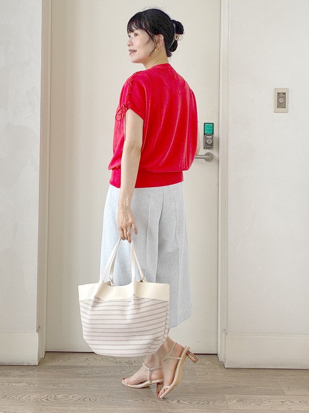 オレンジ系のニット/セーター、グレー系のその他パンツ、ベージュ系のトートバッグを着用したレディースの夏コーディネートの4枚目の写真