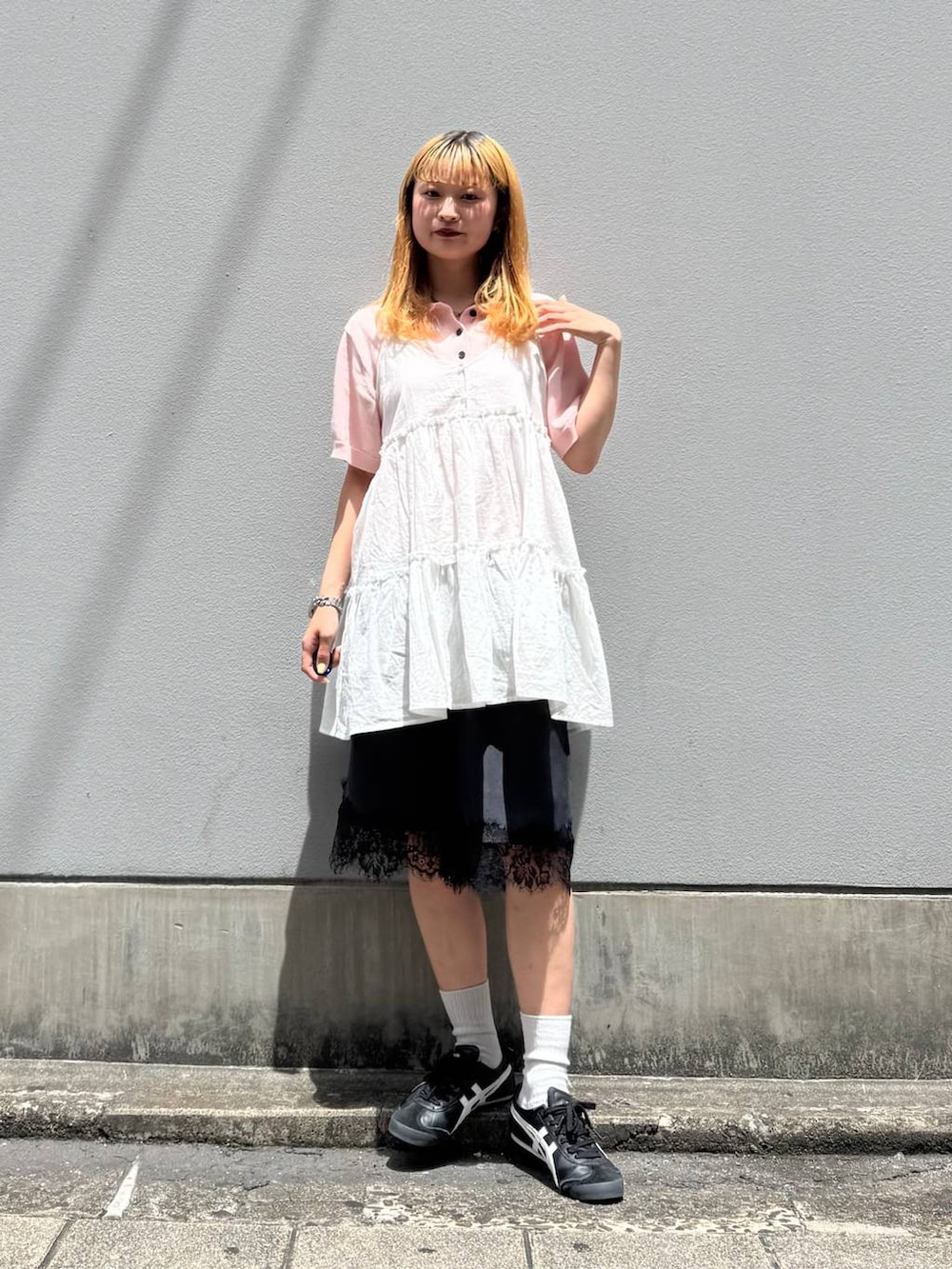 ピンク系のポロシャツ、ホワイト系のチュニック、ブラック系のスラックスを着用したレディースの春コーディネートの2枚目の写真