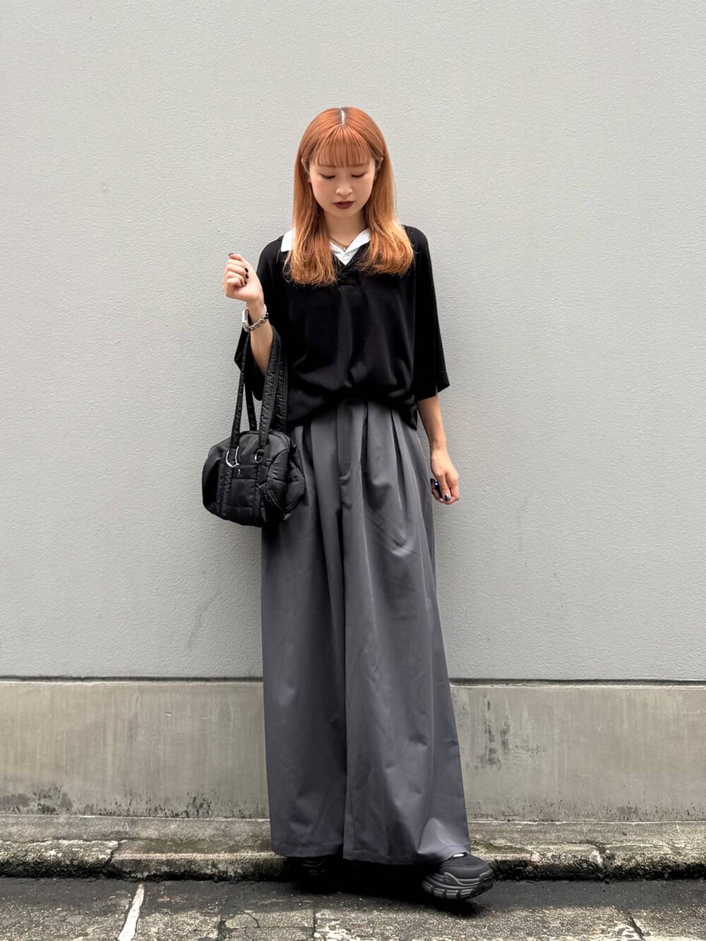 ブラック系のポロシャツ、ブラック系のボストンバッグ、グレー系のスラックスを着用したレディースの夏コーディネートの2枚目の写真
