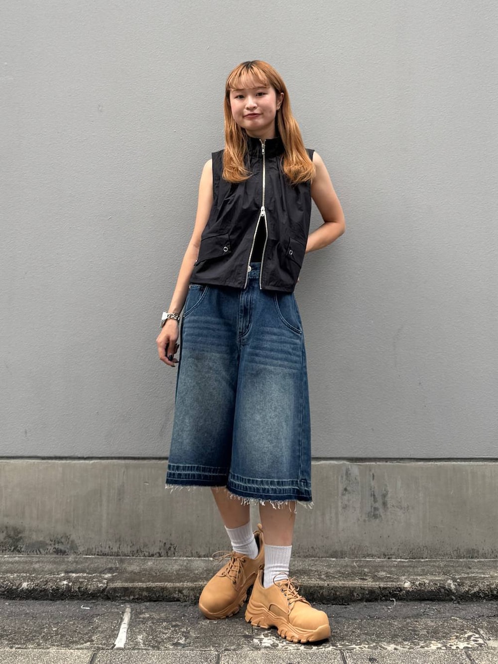 ブルー系のデニムパンツ、イエロー系のブーツ、ブラック系のベストを着用したレディースの夏コーディネートの2枚目の写真