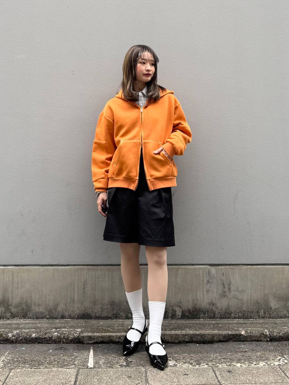 ブラック系のパンプス、ブラック系のスラックス、オレンジ系のパーカーを着用したレディースの春コーディネートの4枚目の写真