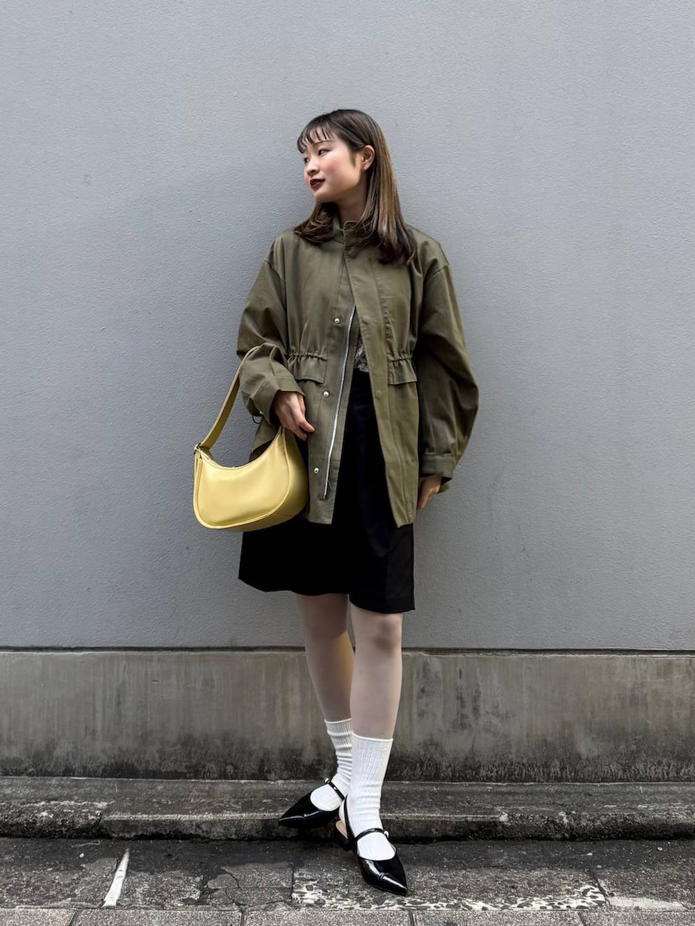 ブラック系のパンプス、ブラック系のスラックス、イエロー系のショルダーバッグを着用したレディースの春コーディネートの2枚目の写真