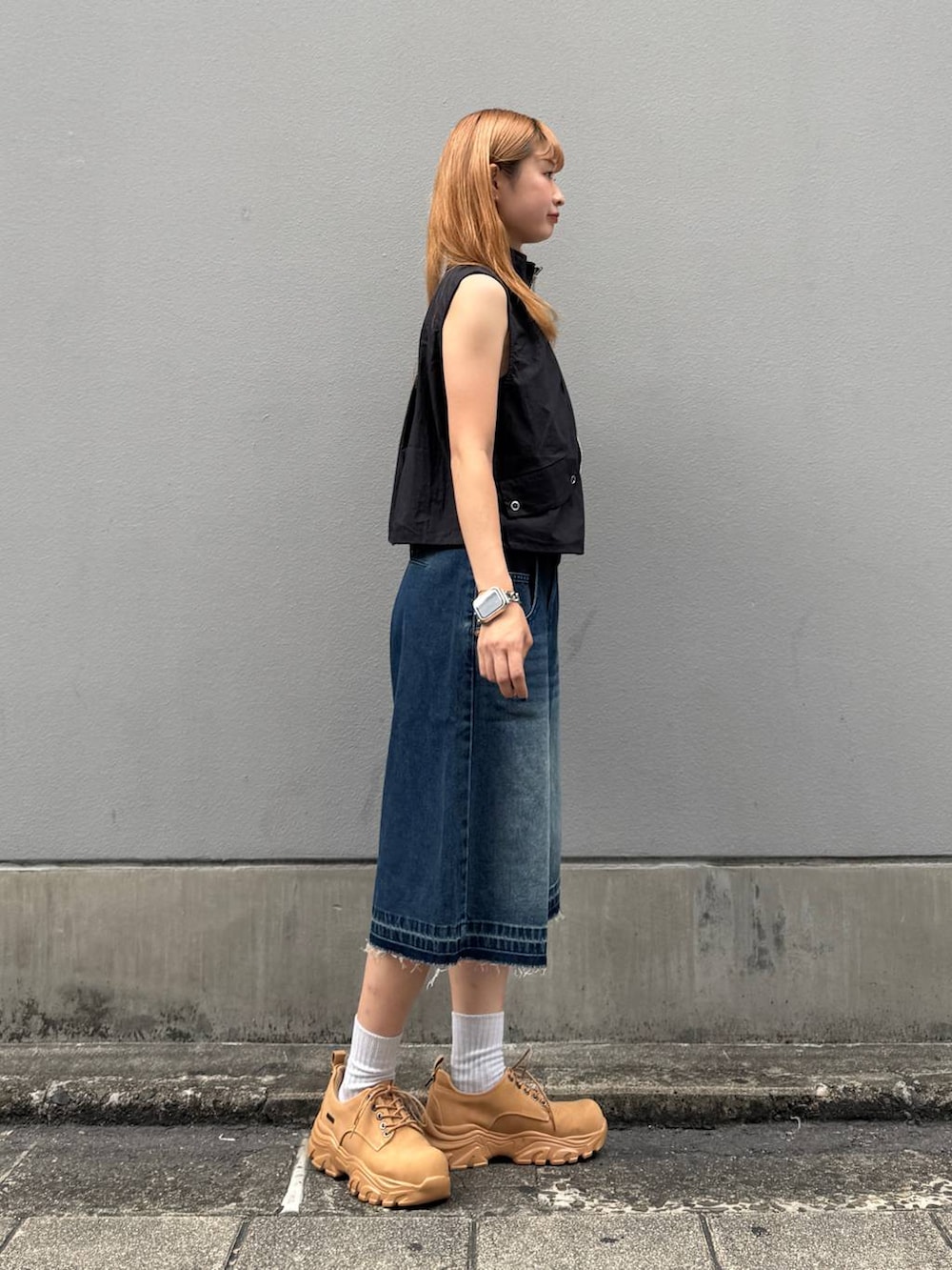 ブルー系のデニムパンツ、イエロー系のブーツ、ブラック系のベストを着用したレディースの夏コーディネートの7枚目の写真