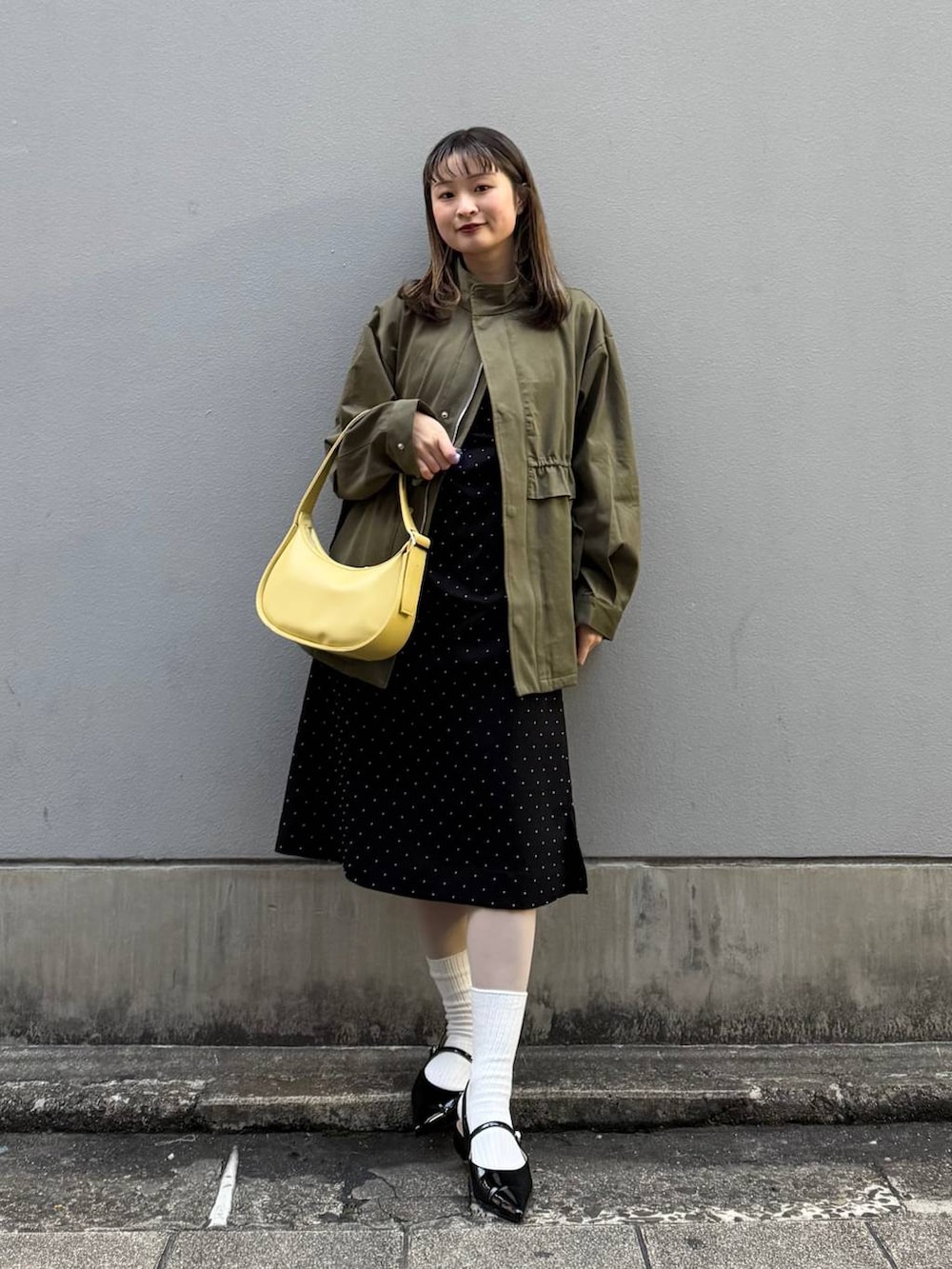 ブラック系のパンプス、イエロー系のショルダーバッグ、ブラック系のワンピースを着用したレディースの春コーディネートの4枚目の写真
