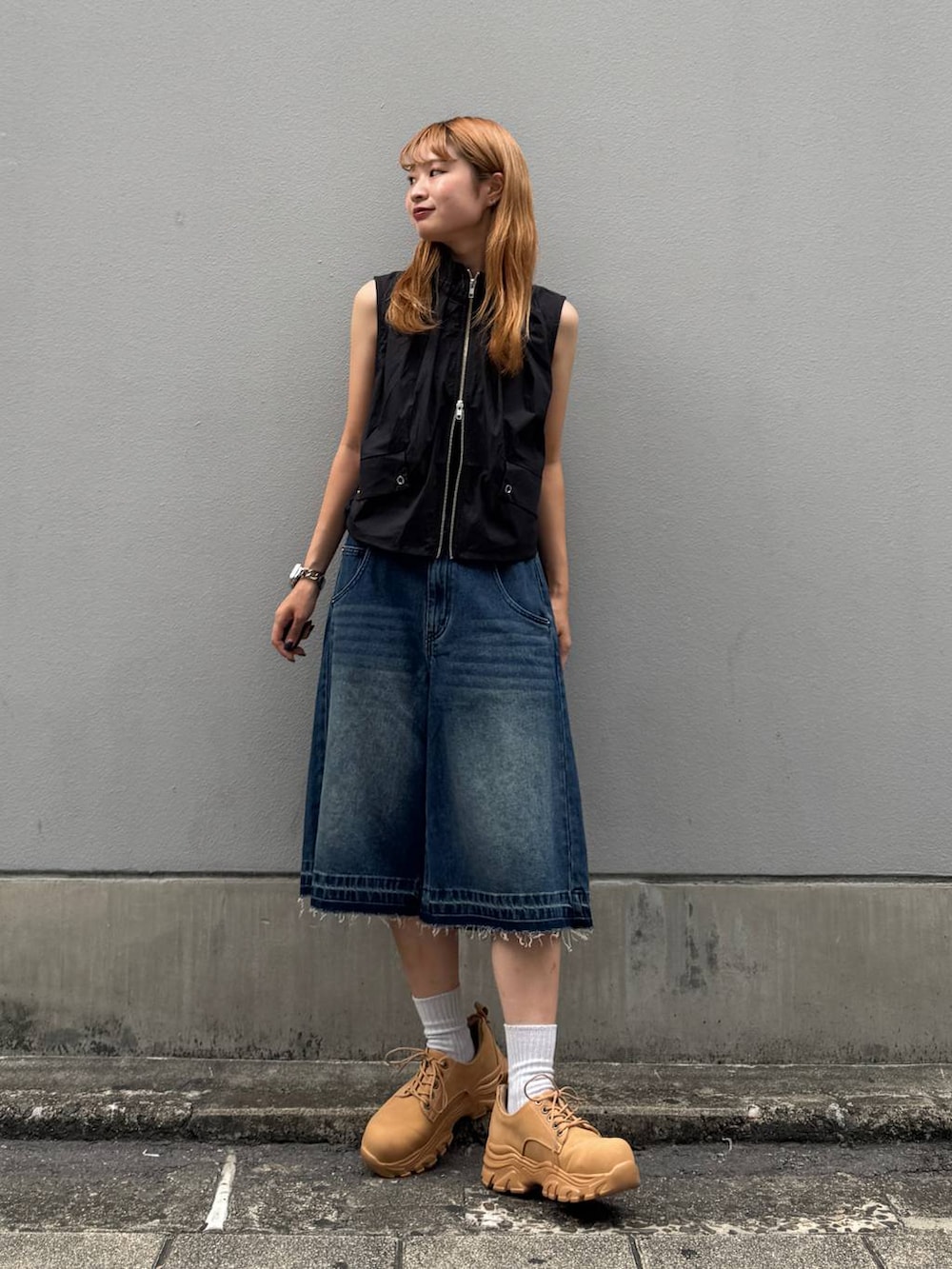 ブルー系のデニムパンツ、イエロー系のブーツ、ブラック系のベストを着用したレディースの夏コーディネートの3枚目の写真