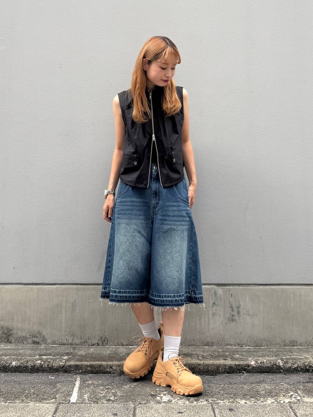 ブルー系のデニムパンツ、イエロー系のブーツ、ブラック系のベストを着用したレディースの夏コーディネートの4枚目の写真
