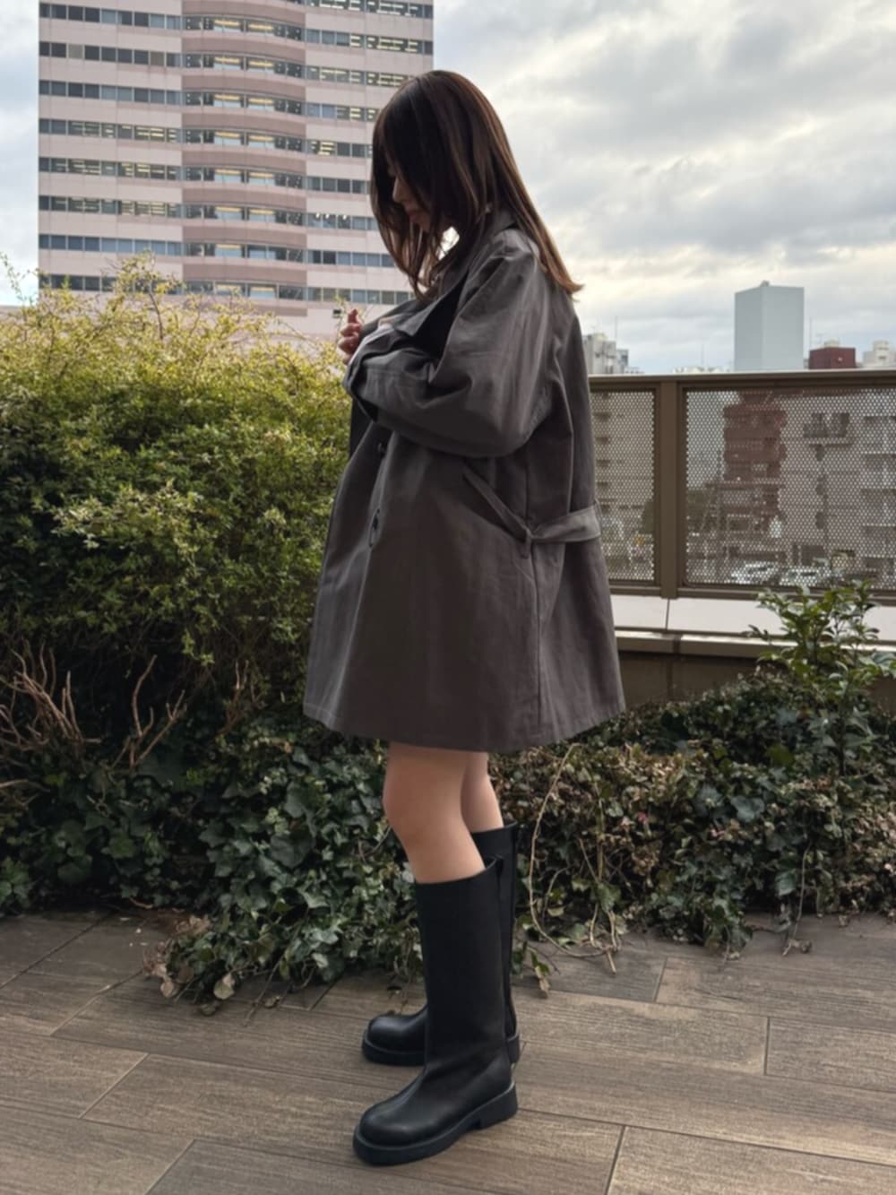 ホワイト系のシャツ/ブラウス、ブラック系のブーツ、グレー系のトレンチコートを着用したレディースの春コーディネートの2枚目の写真