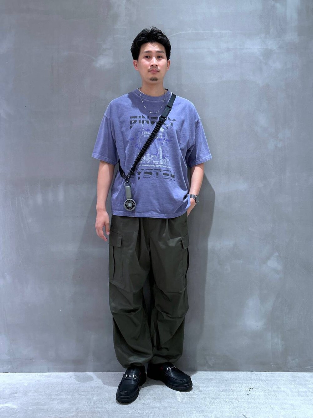 ブラック系のローファー、グリーン系のカーゴパンツ、ブラック系のスマホグッズを着用したメンズの夏コーディネートの2枚目の写真