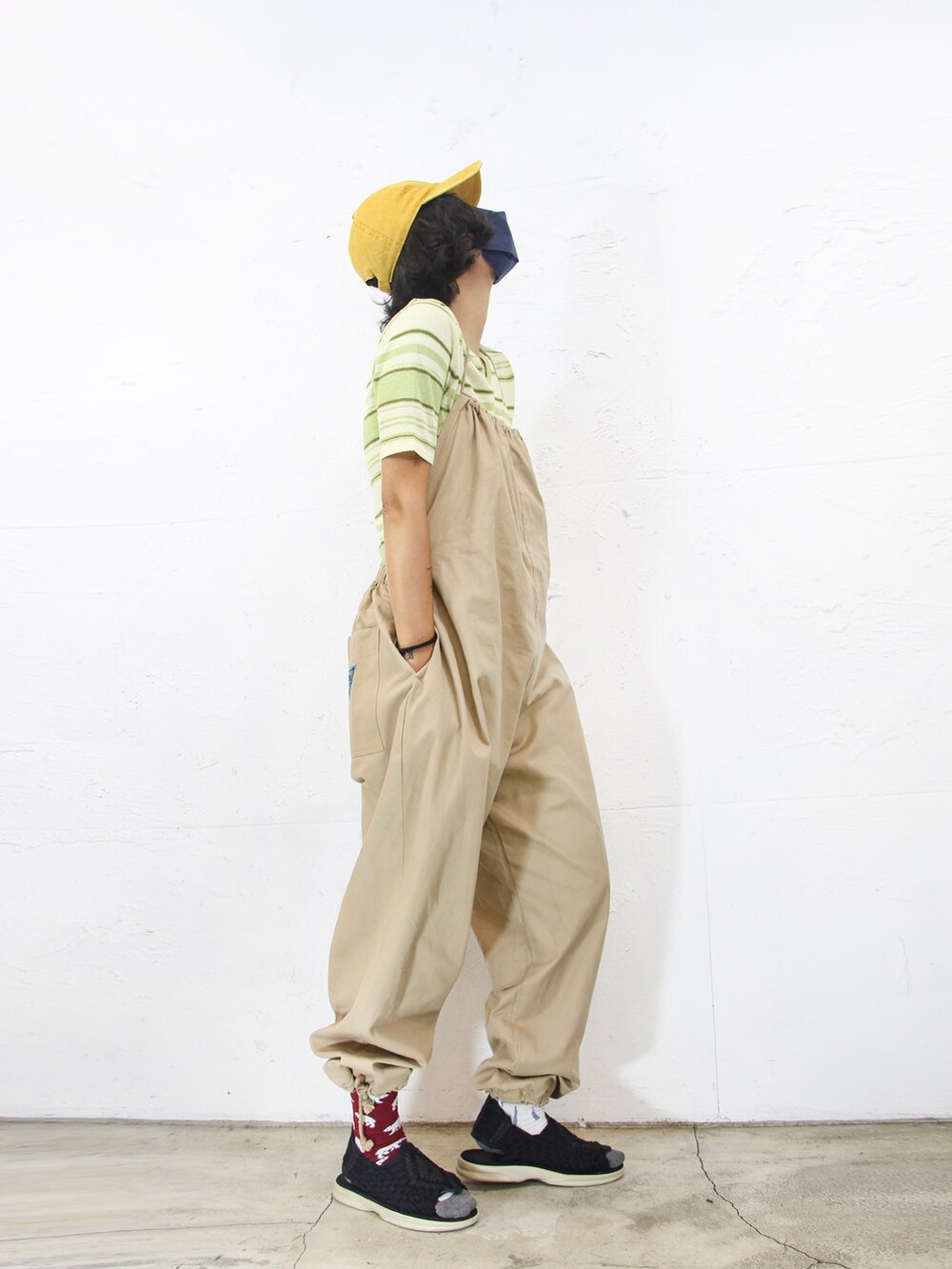 グリーン系のニット/セーター、ベージュ系のサロペット/オーバーオール、イエロー系のキャップを着用したレディースの夏コーディネートの2枚目の写真