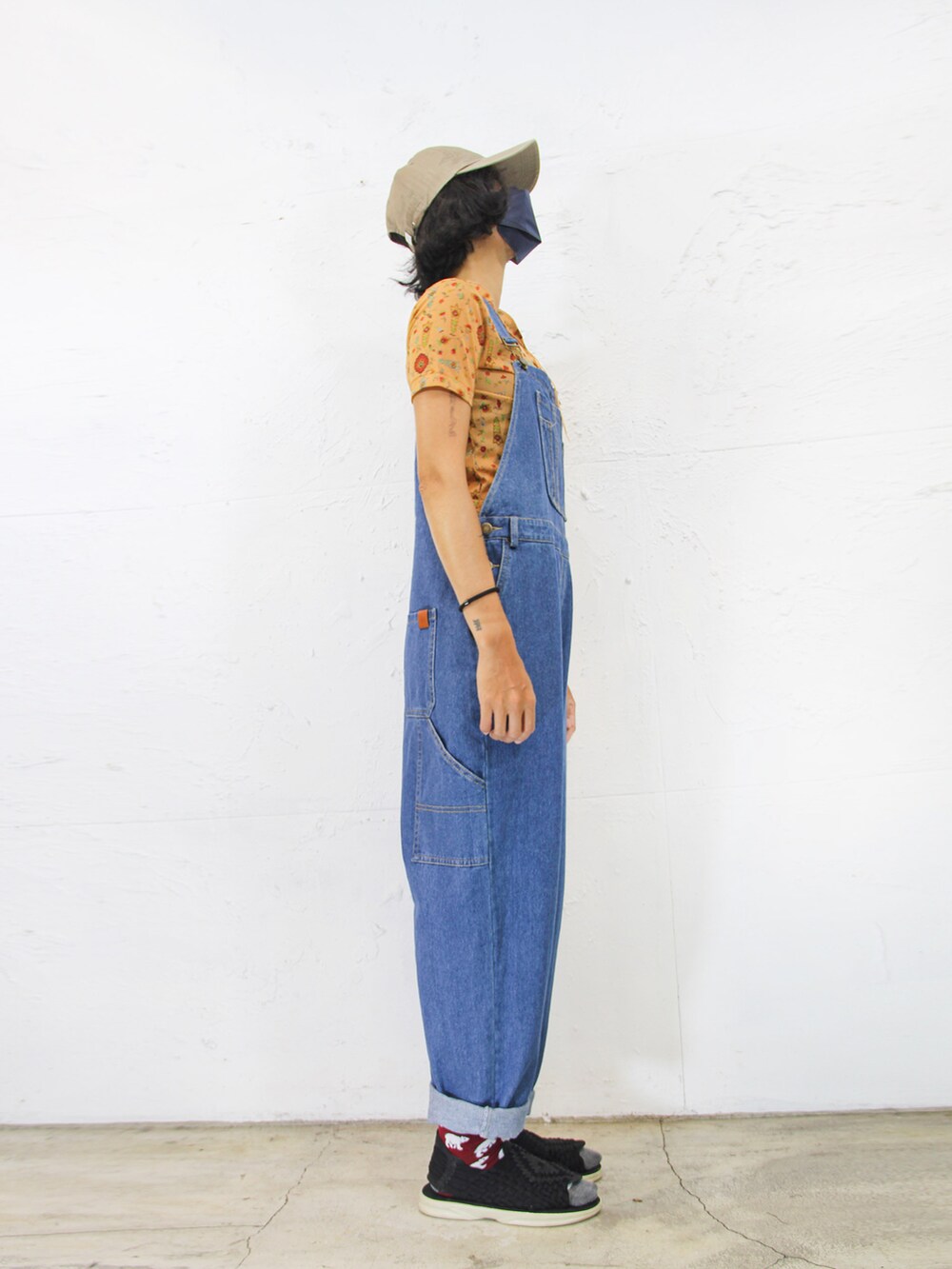 ブルー系のつなぎ/オールインワン、オレンジ系のトップス、ベージュ系のキャップを着用したレディースの夏コーディネートの5枚目の写真