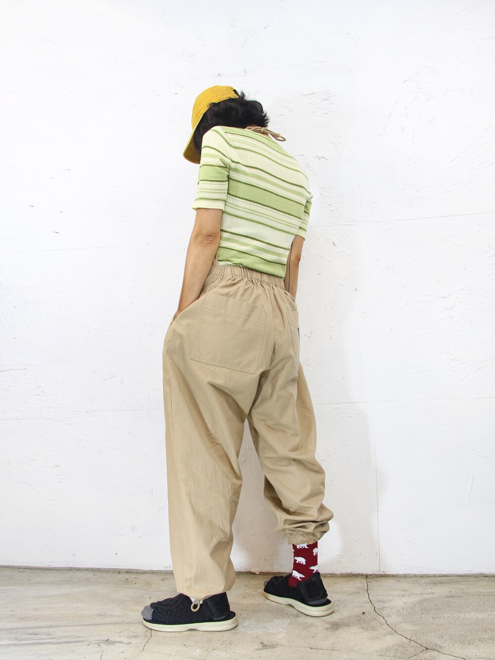 グリーン系のニット/セーター、ベージュ系のサロペット/オーバーオール、イエロー系のキャップを着用したレディースの夏コーディネートの3枚目の写真