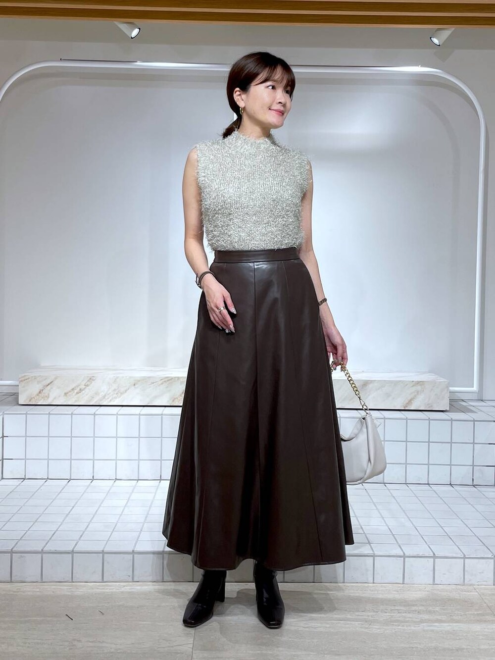 ブラウン系のブーツ、グレー系のニット/セーター、ホワイト系のショルダーバッグを着用したレディースの秋コーディネートの2枚目の写真