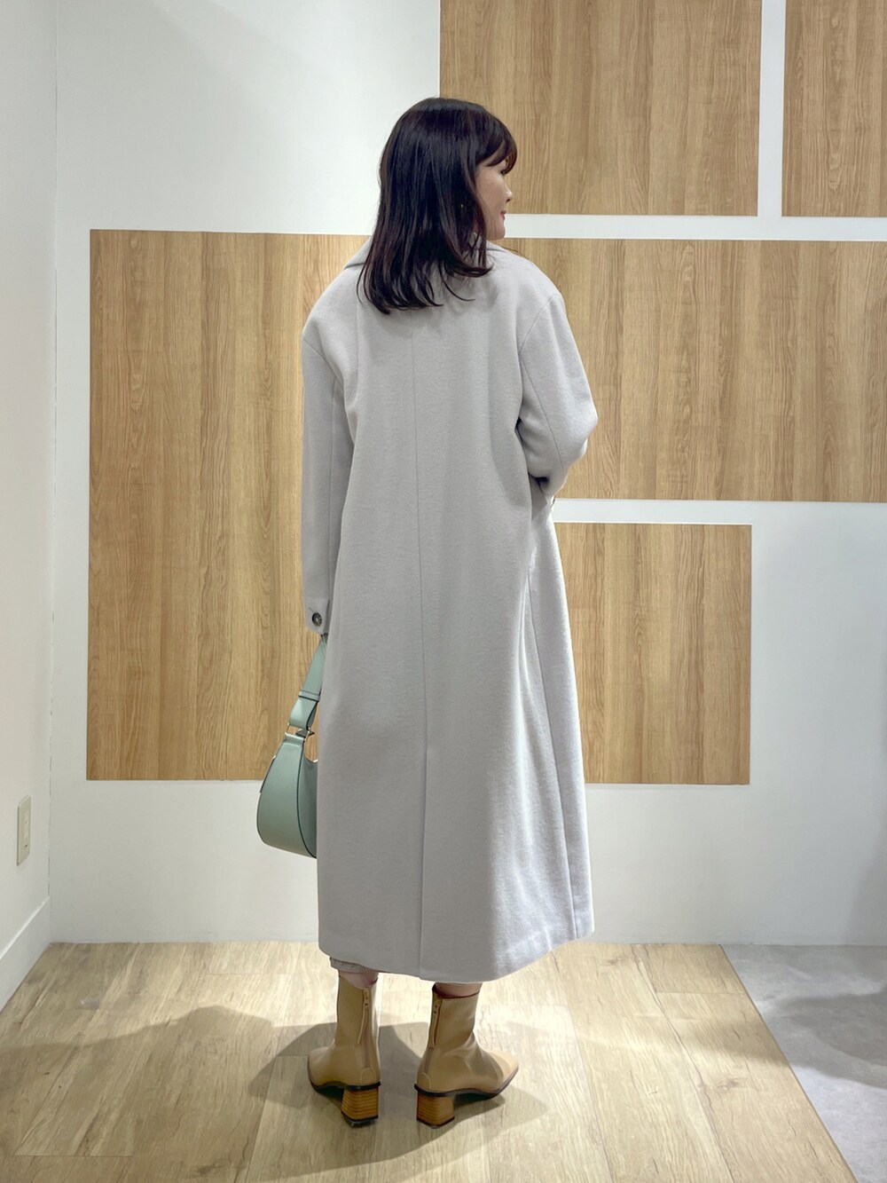 グレー系のチェスターコート、グレー系のワンピース、グリーン系のショルダーバッグを着用したレディースの冬コーディネートの3枚目の写真