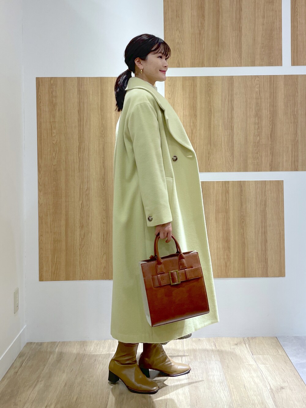 イエロー系のニット/セーター、グリーン系のチェスターコート、グレー系のスカートを着用したレディースの秋コーディネートの2枚目の写真