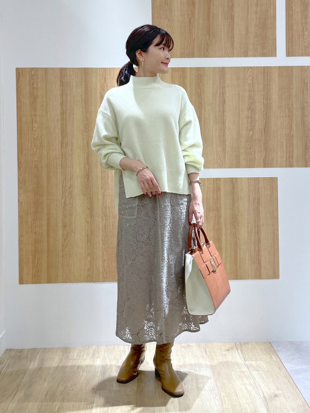 イエロー系のニット/セーター、グリーン系のチェスターコート、グレー系のスカートを着用したレディースの秋コーディネートの4枚目の写真