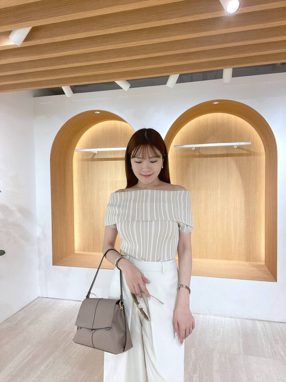 ホワイト系のサンダル、ホワイト系のスラックス、ブラウン系のハンドバッグを着用したレディースの夏コーディネートの2枚目の写真