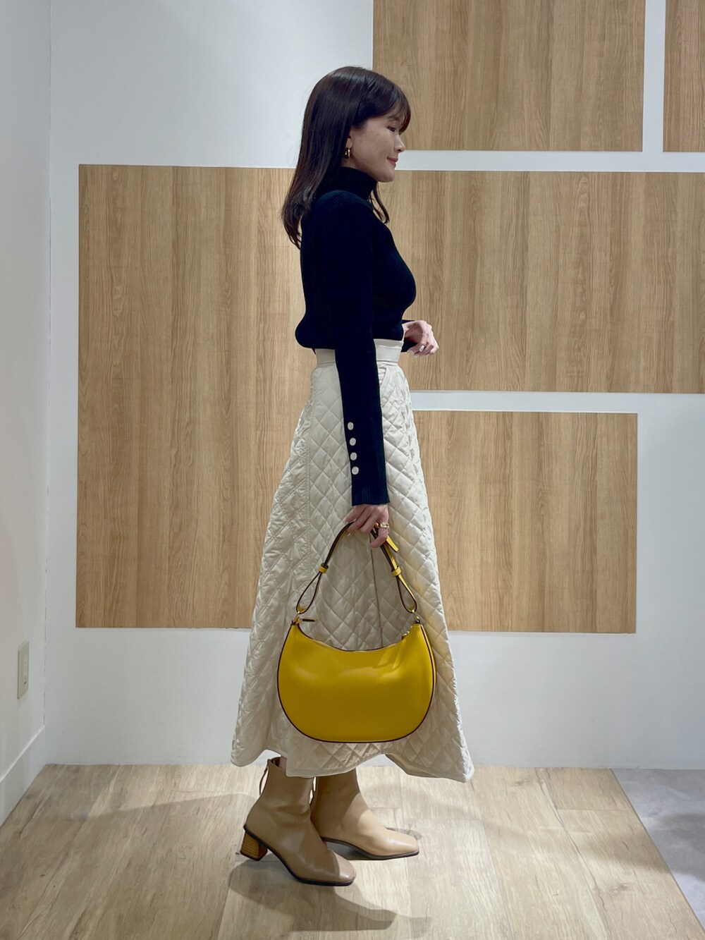 ブラック系のニット/セーター、ベージュ系のスカート、イエロー系のショルダーバッグを着用したレディースの冬コーディネートの2枚目の写真