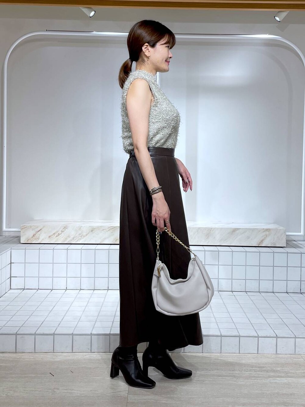 ブラウン系のブーツ、グレー系のニット/セーター、ホワイト系のショルダーバッグを着用したレディースの秋コーディネートの3枚目の写真