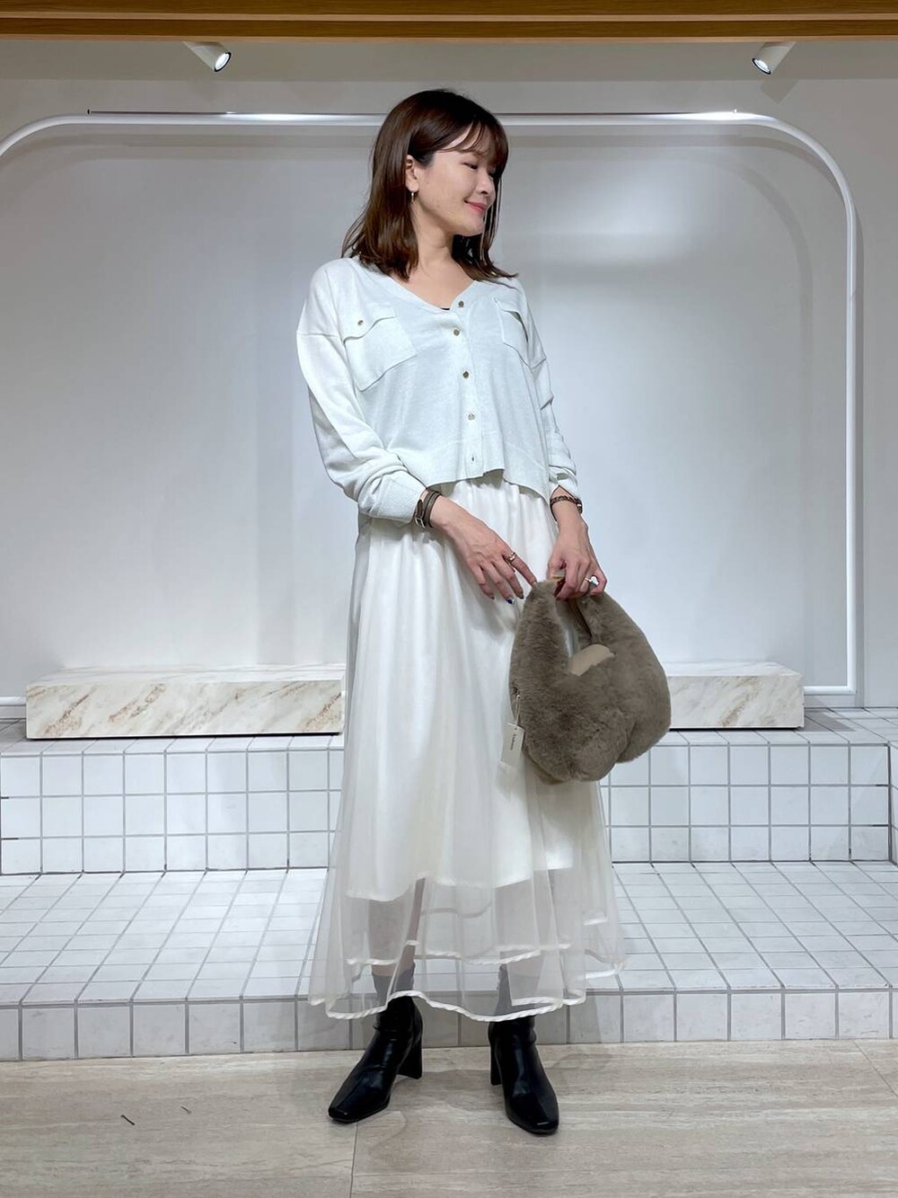 ホワイト系のスカート、ブラック系のブーツ、ホワイト系のカーディガン/ボレロを着用したレディースの秋コーディネートの2枚目の写真