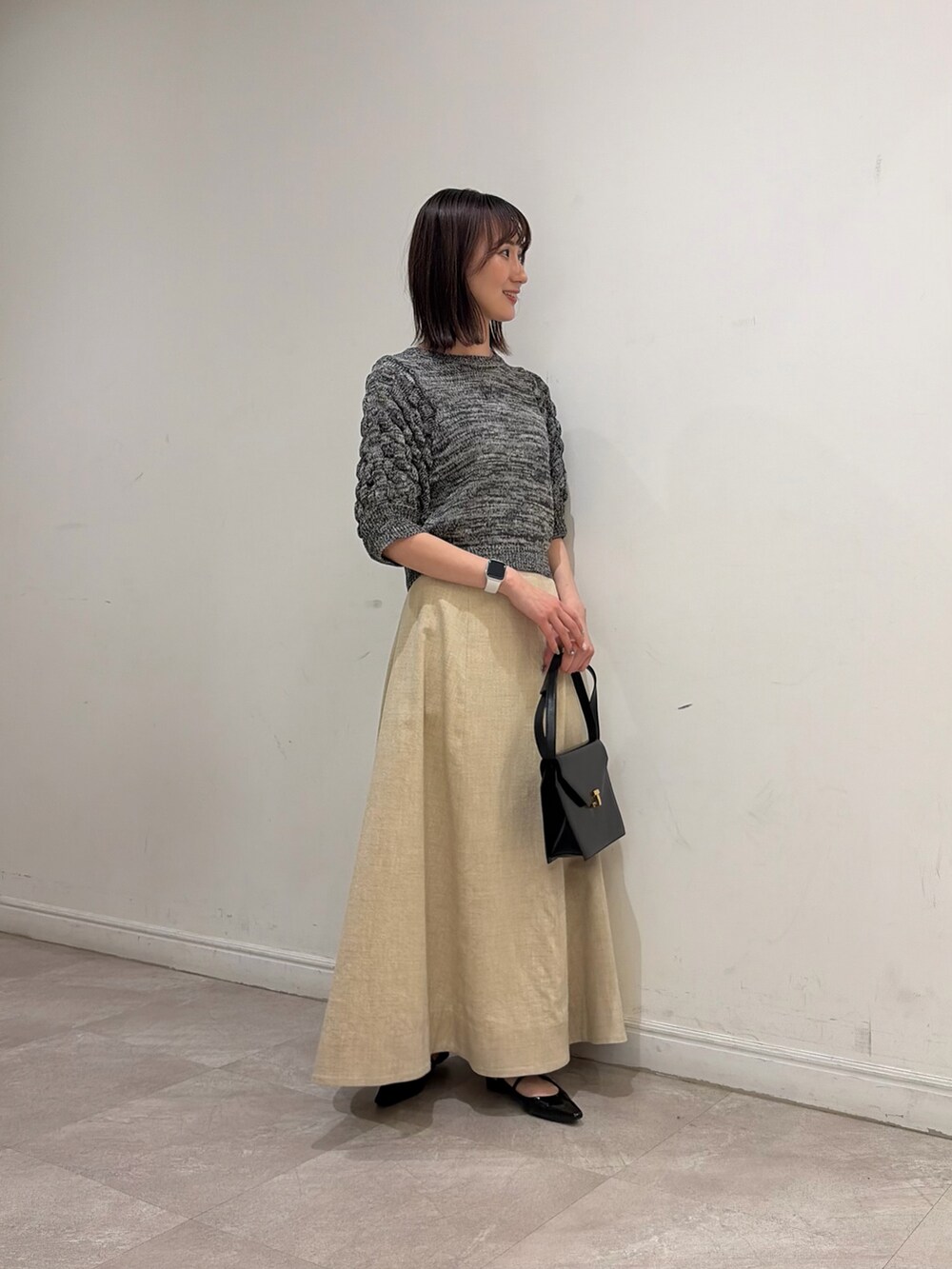 グレー系のニット/セーター、ベージュ系のスカート、ブラック系のパンプスを着用したレディースの春コーディネートの2枚目の写真