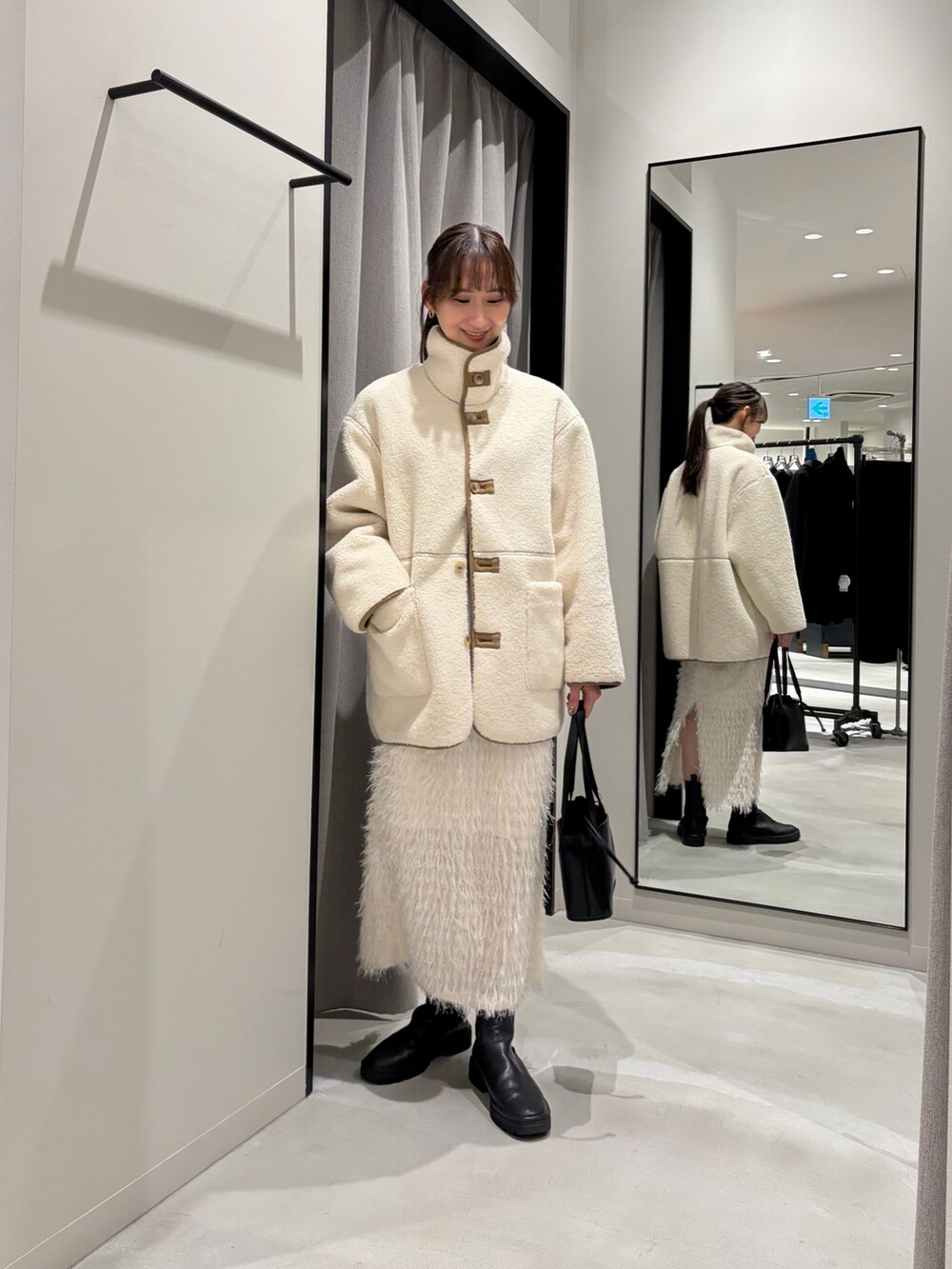 ホワイト系のムートンコート、ブルー系のニット/セーター、ホワイト系のTシャツ/カットソーを着用したレディースの冬コーディネートの2枚目の写真