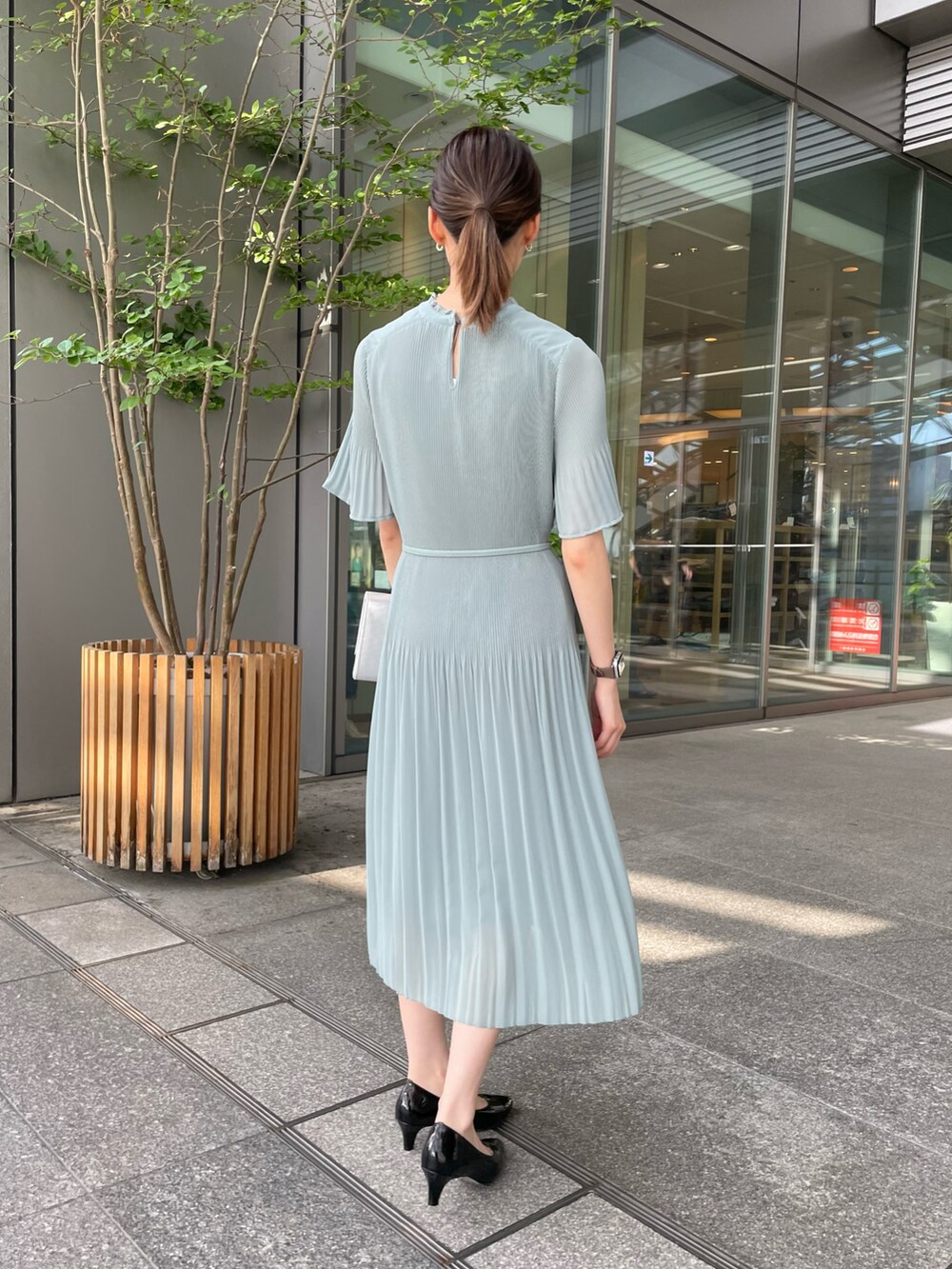 シルバー系のクラッチバッグ、ブラック系のパンプス、グリーン系のワンピースを着用したレディースの夏コーディネートの2枚目の写真