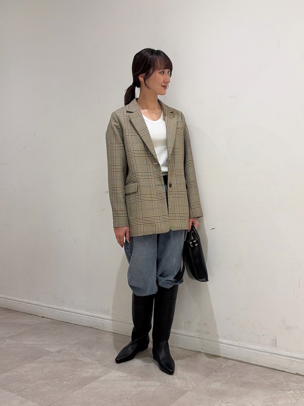 ブルー系のデニムパンツ、ブラック系のブーツ、ブラック系のショルダーバッグを着用したレディースの秋コーディネートの2枚目の写真