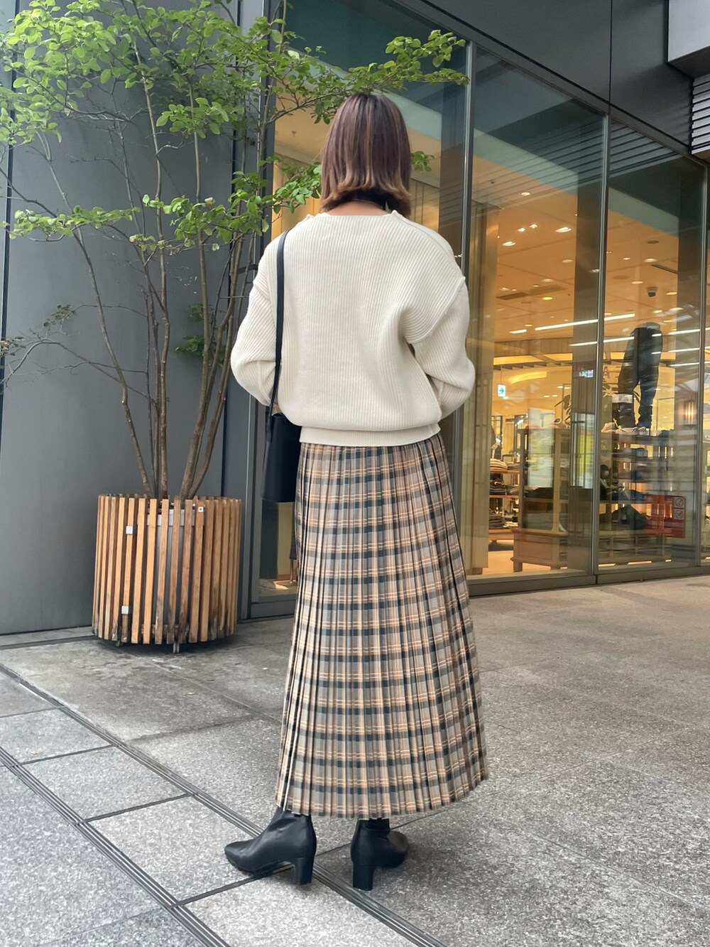 グリーン系のスカート、ホワイト系のニット/セーター、ブラック系のブーツを着用したレディースの秋コーディネートの2枚目の写真