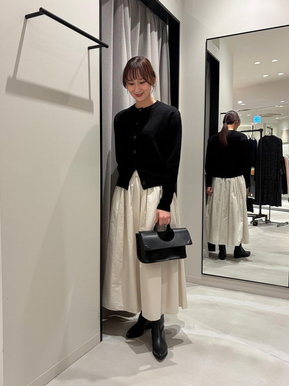 ブラック系のカーディガン/ボレロ、ホワイト系のスカート、ブラック系のハンドバッグを着用したレディースの冬コーディネートの2枚目の写真