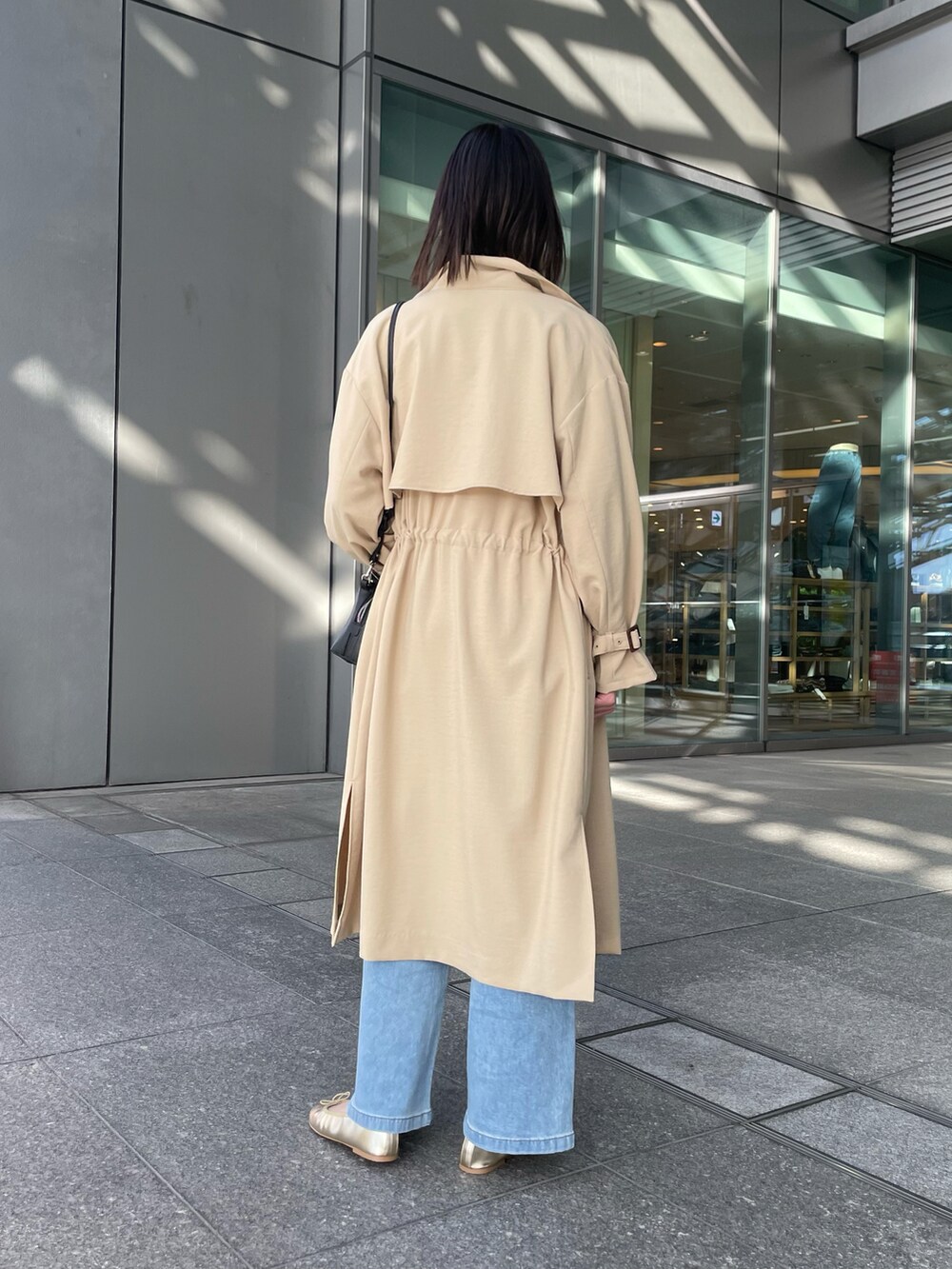 ベージュ系のトレンチコート、ブラック系のショルダーバッグ、ブルー系のデニムパンツを着用したレディースの冬コーディネートの3枚目の写真