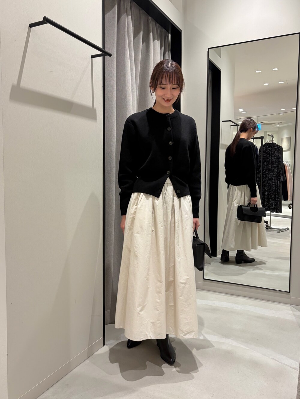 ブラック系のカーディガン/ボレロ、ホワイト系のスカート、ブラック系のハンドバッグを着用したレディースの冬コーディネートの3枚目の写真