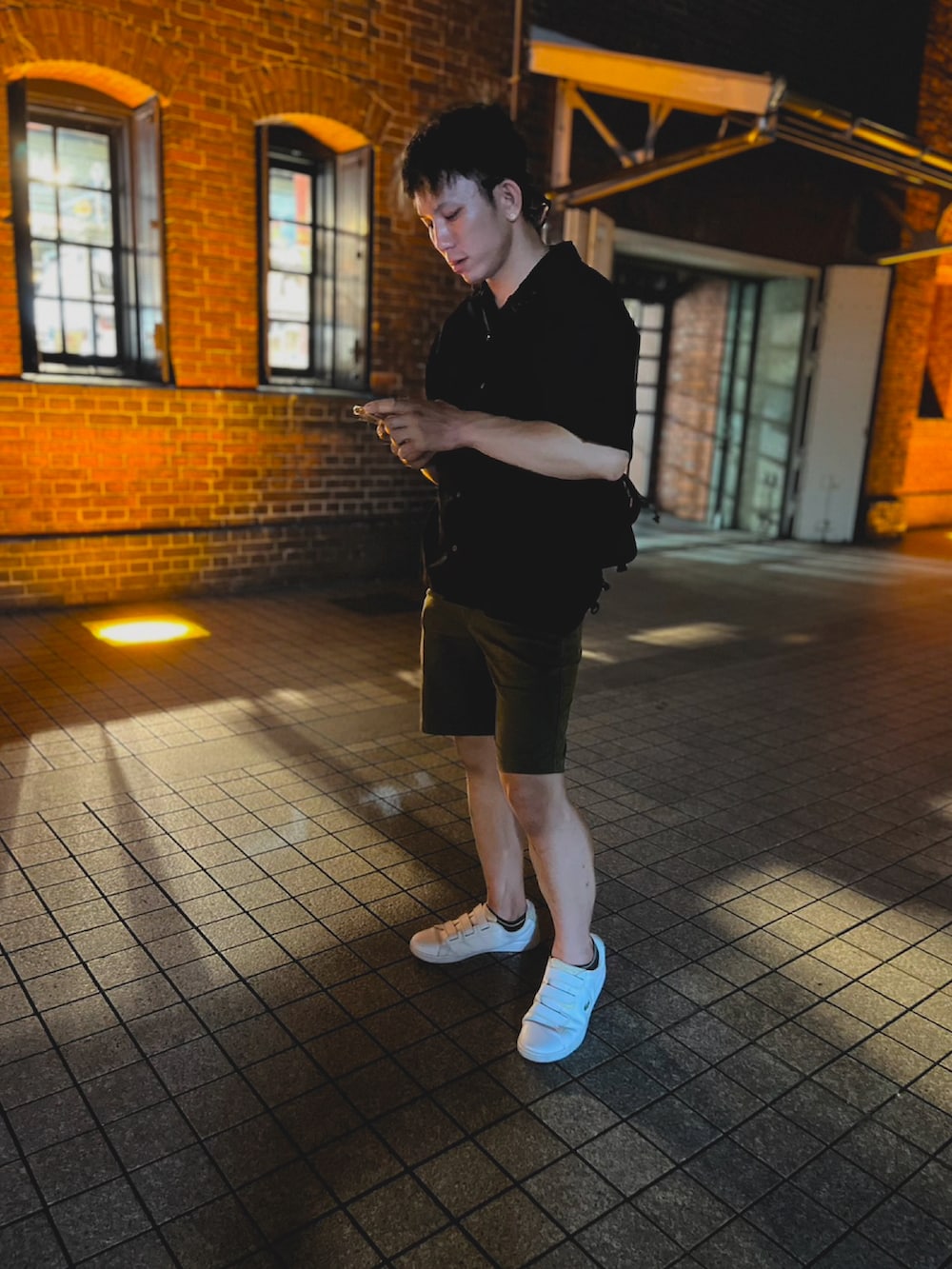 ホワイト系のスニーカー、ブラック系のシャツ/ブラウス、グリーン系のチノパンツを着用したメンズの夏コーディネートの2枚目の写真