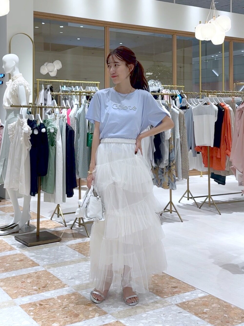 ホワイト系のトートバッグ、ホワイト系のスカート、ブルー系のTシャツ/カットソーを着用したレディースの夏コーディネートの4枚目の写真