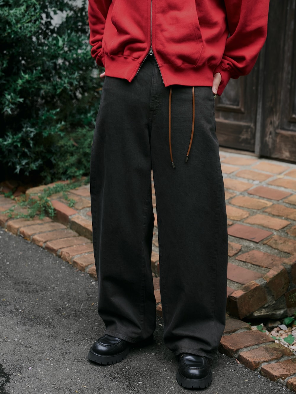 レッド系のパーカー、ブラウン系のデニムパンツ、ブラック系のキャップを着用したメンズの秋コーディネートの3枚目の写真