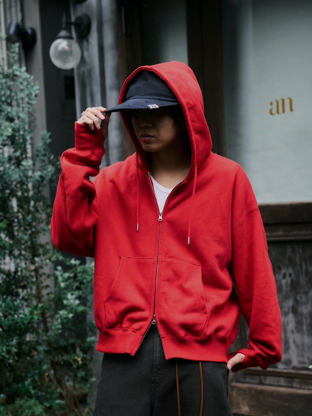 レッド系のパーカー、ブラウン系のデニムパンツ、ブラック系のキャップを着用したメンズの秋コーディネートの2枚目の写真