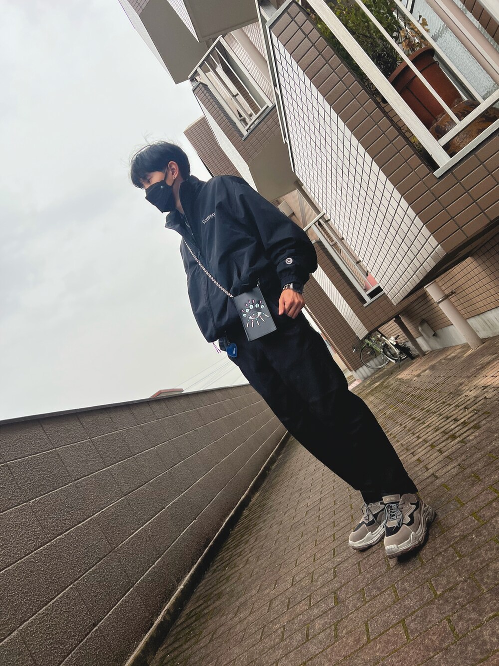 ブラック系のナイロンジャケット、ブラック系のショルダーバッグ、ブラック系のスラックスを着用したメンズの冬コーディネートの2枚目の写真