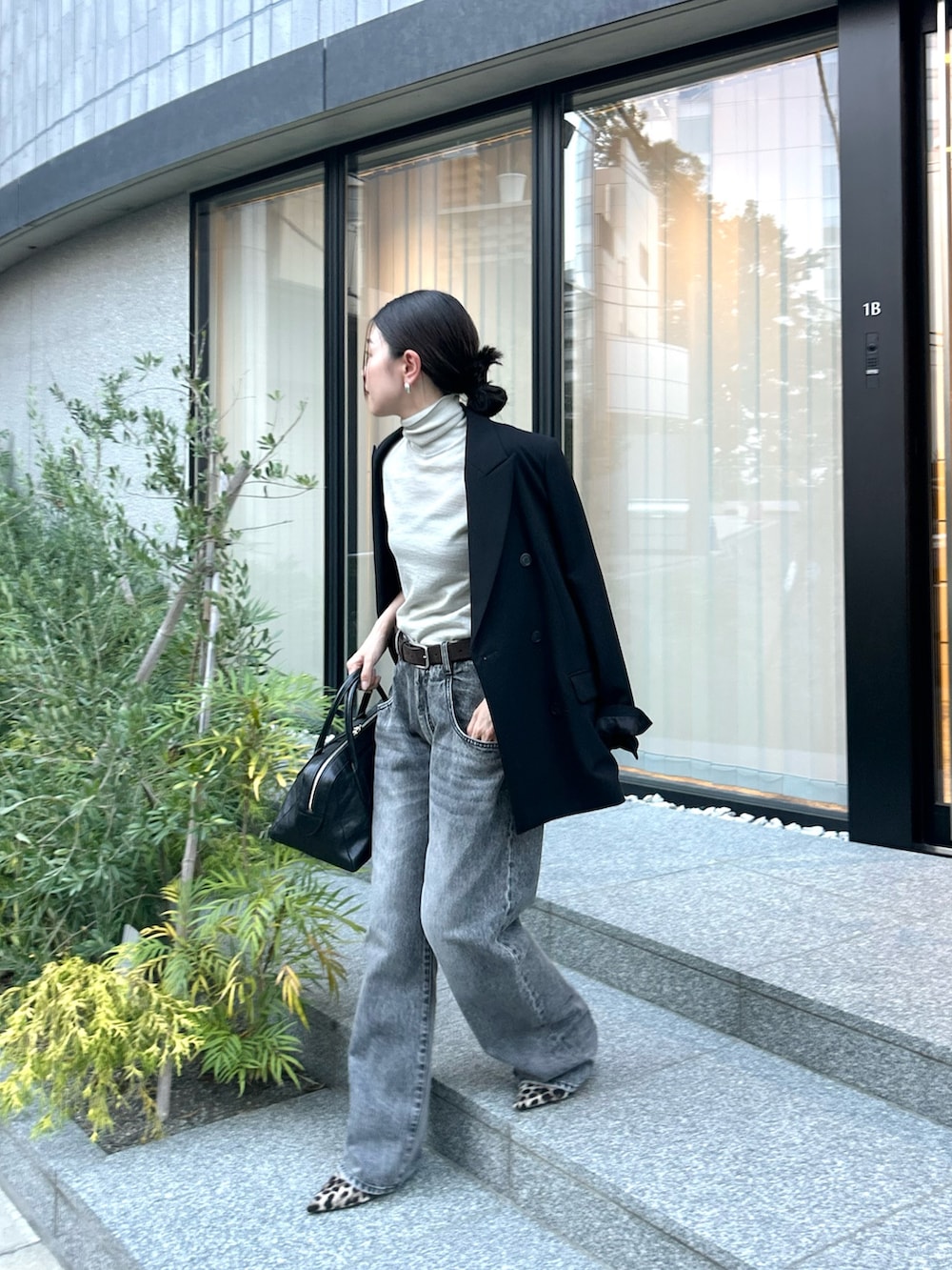ブラック系のテーラードジャケット、ブラック系のトートバッグ、グレー系のデニムパンツを着用したレディースの秋コーディネートの2枚目の写真