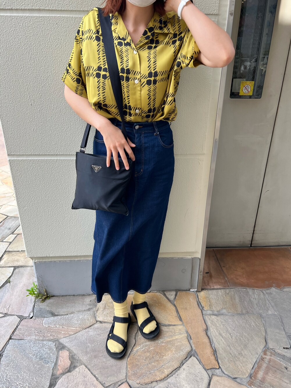 ブラック系のサンダル、ブルー系のデニムスカート、ブラック系のショルダーバッグを着用したレディースの春コーディネートの3枚目の写真