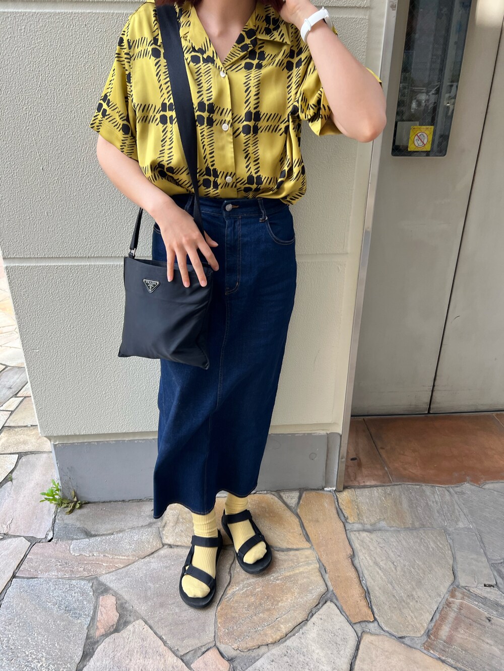 ブラック系のサンダル、ブルー系のデニムスカート、ブラック系のショルダーバッグを着用したレディースの春コーディネートの2枚目の写真