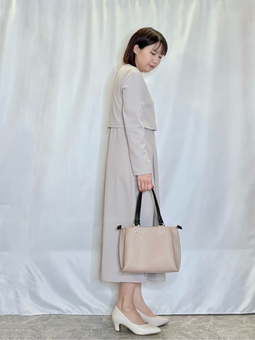グレー系のワンピース、ホワイト系のパンプス、ベージュ系のトートバッグを着用したレディースの春コーディネートの2枚目の写真