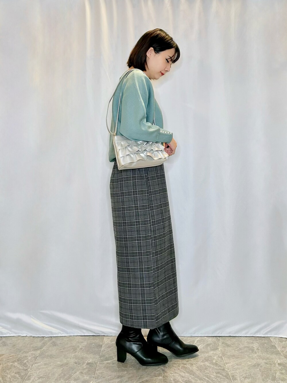 ブラック系のブーツ、シルバー系のショルダーバッグ、ブラック系のスカートを着用したレディースの秋コーディネートの2枚目の写真