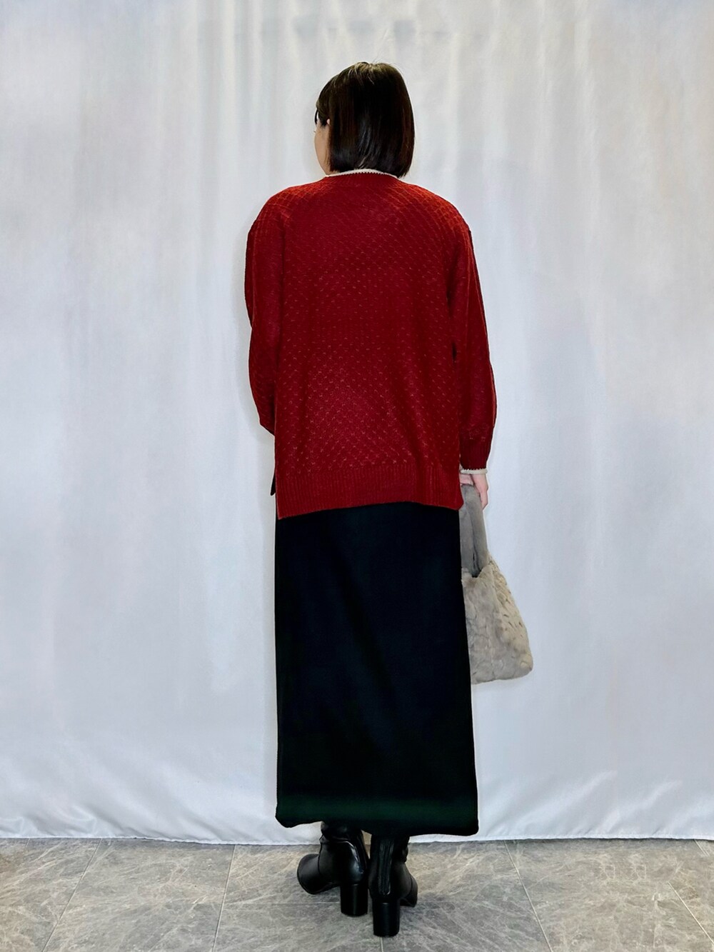 レッド系のニット/セーター、ベージュ系のトートバッグ、ブラック系のスカートを着用したレディースの冬コーディネートの3枚目の写真