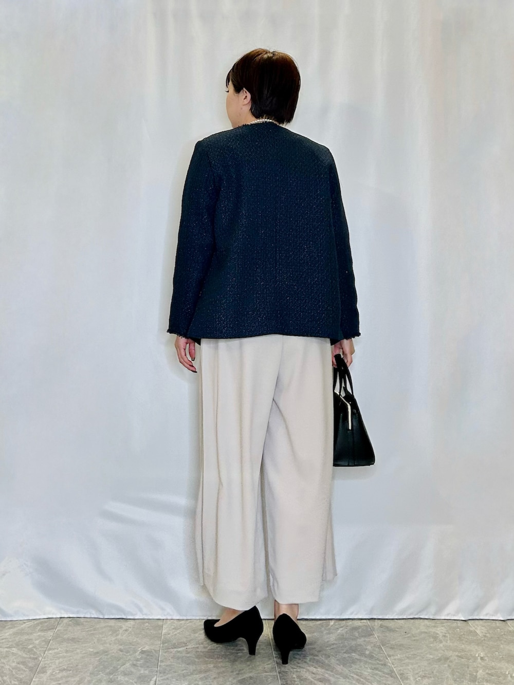 ブラック系のトートバッグ、ブラック系のパンプス、ブルー系のノーカラージャケットを着用したレディースの春コーディネートの3枚目の写真