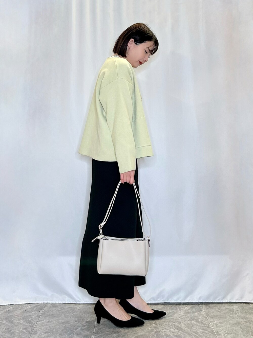 ブラック系のパンプス、ブラック系のスカート、ベージュ系のショルダーバッグを着用したレディースの春コーディネートの2枚目の写真